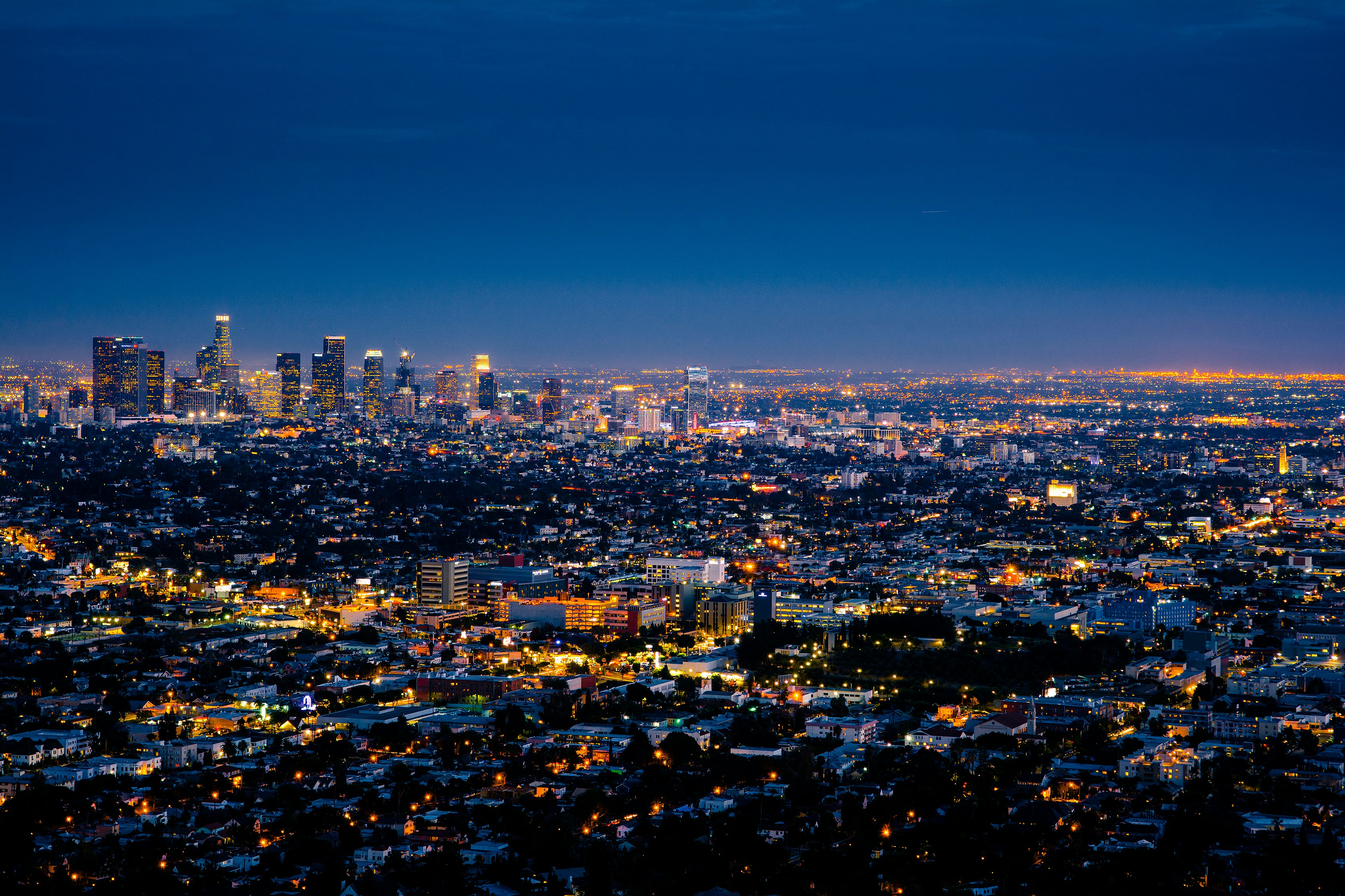 Los Angeles basin at night, downtown towers lit against a blue dusk sky