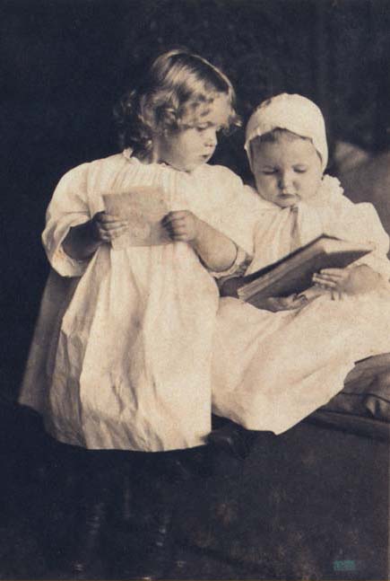 Archival photograph of two young children in white dresses reading