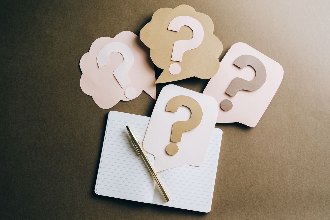 Open notebook with a pen and paper speech bubbles printed with question marks