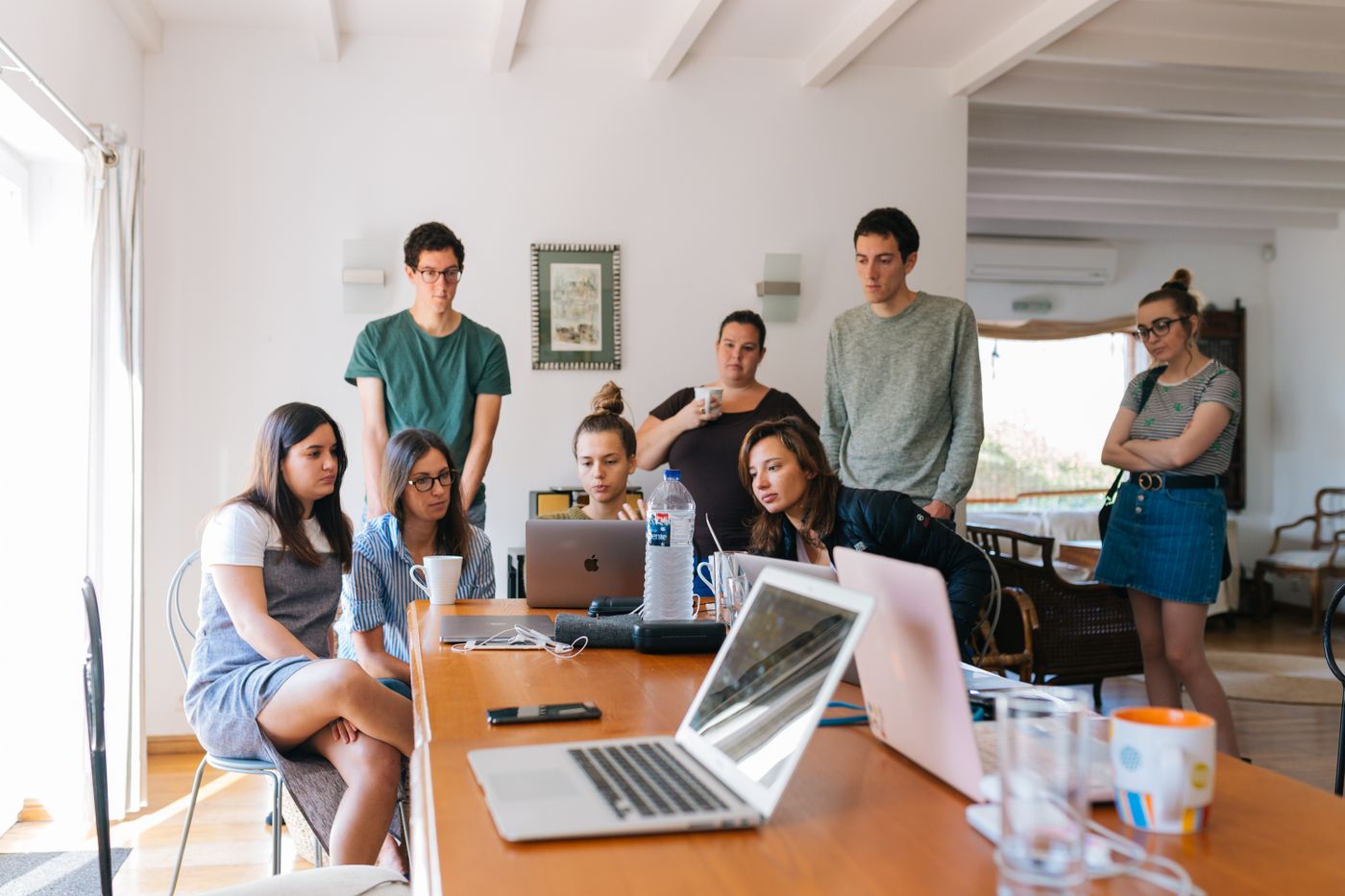 Group of young adults gathered around laptops at a long wooden table