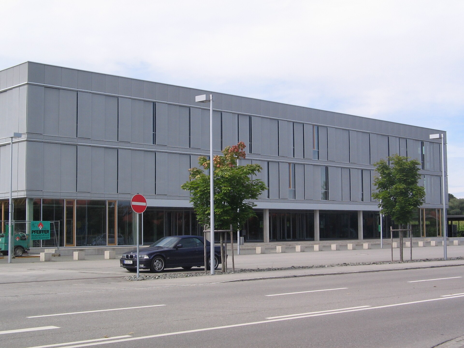 Modern three-story hall with a glass ground floor and a parked car on the street
