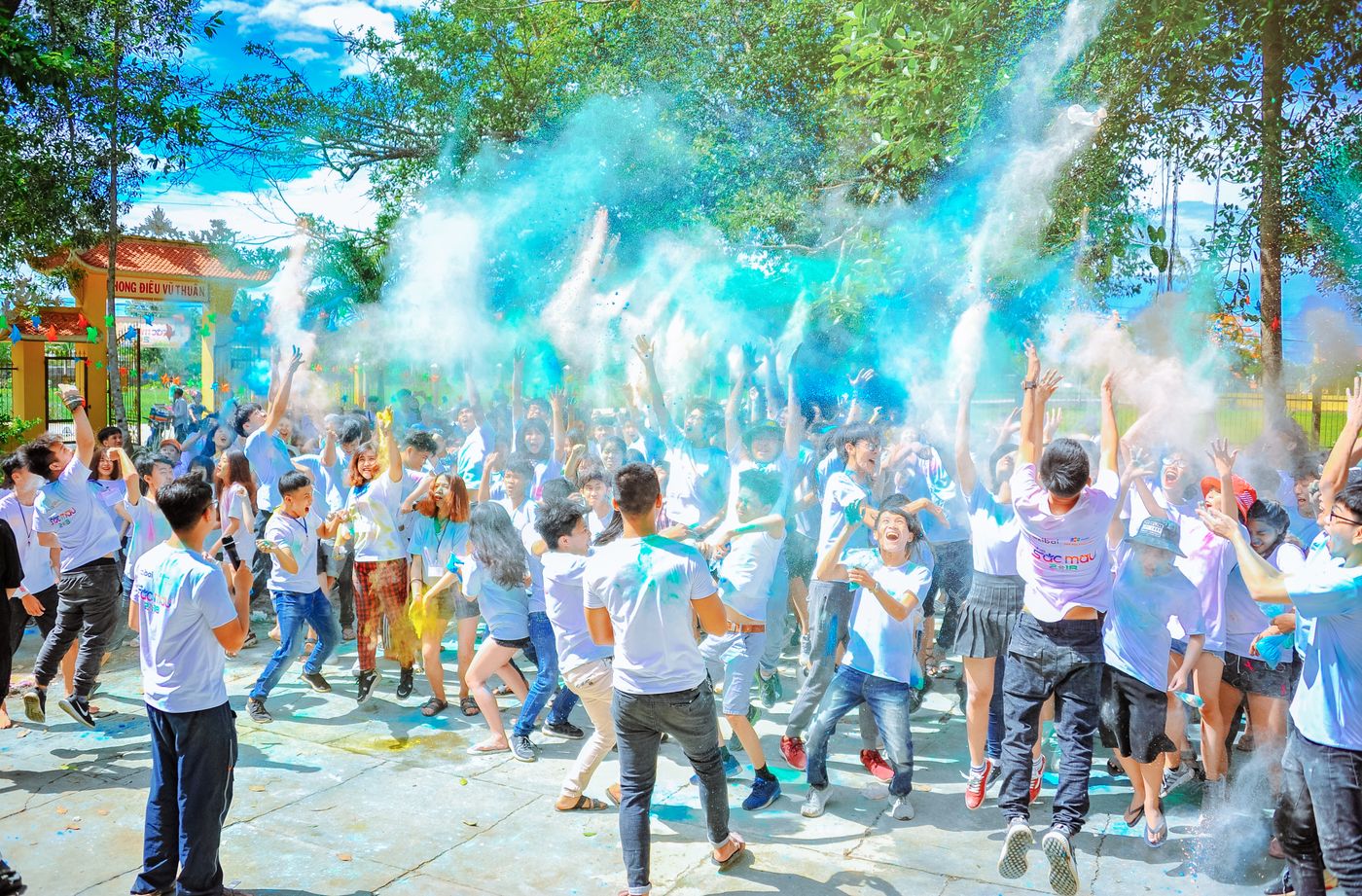 Crowd in white shirts throwing blue color powder in an outdoor courtyard